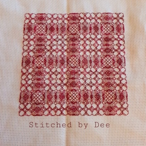 May include: A red cross stitch pattern on white Aida cloth with the text "Stitched by Dee" at the bottom.