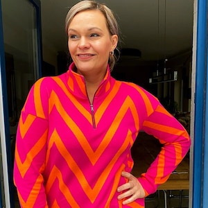 Könnte beinhalten: Ein langärmliges Shirt mit einem Chevron-Muster in Pink und Orange, mit einem Reißverschluss am Kragen.