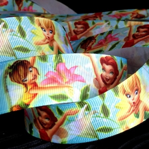 May include: A blue ribbon with a repeating pattern of fairies and flowers. The fairies are wearing colourful dresses and have wings. The flowers are pink, yellow, and red.