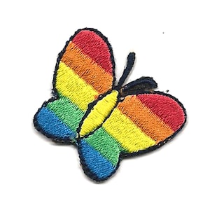 May include: Embroidered butterfly patch in rainbow colours. The butterfly has a black outline and is filled with horizontal stripes of red, orange, yellow, green, blue, and purple. The patch is on a white background.