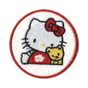 Peut inclure: Un patch brodé rond avec une bordure rouge représentant Hello Kitty tenant un petit ours jaune.