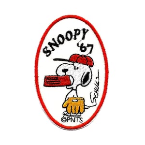 Può includere: Toppa ricamata ovale con bordo rosso, raffigurante Snoopy dei Peanuts. Snoopy tiene in mano una radio rossa, indossa un berretto rosso e un guanto giallo. È incluso il testo "SNOOPY '67", oltre alla firma di Charles Schulz.
