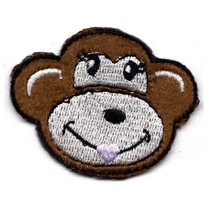 May include: Brown embroidered monkey face with white eyes, a white nose, and a pink tongue. The monkey is smiling.