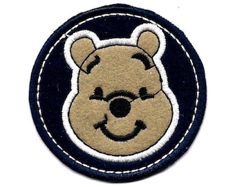 May include: A blue and white embroidered patch featuring a cartoon Winnie the Pooh bear with a smiling face.
