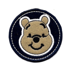 May include: A blue and white embroidered patch featuring a cartoon Winnie the Pooh bear with a smiling face.
