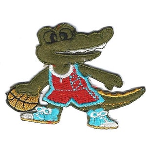 May include: An embroidered patch of a green alligator wearing a red basketball uniform and holding a basketball. The alligator is wearing blue and white sneakers.