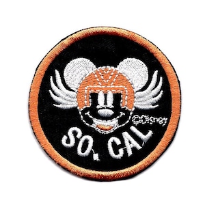 May include: A round, orange and black embroidered patch featuring a cartoon mouse wearing a football helmet and wings. The text "SO. CAL" is below the mouse.