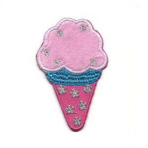 Puede incluir: Cono de helado rosa y azul con estrellas plateadas brillantes. El helado es rosa y el cono es rosa con una banda azul.