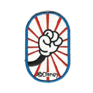 May include: A blue and white oval-shaped embroidered patch with a red and white sunburst design. A black and white cartoon hand is raised in a fist with the text "©Disney" at the bottom.