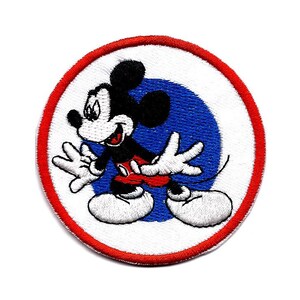 May include: A red and white circular embroidered patch with a blue circle in the center. Mickey Mouse is depicted in black and white, wearing red shorts, and is standing on the blue circle.