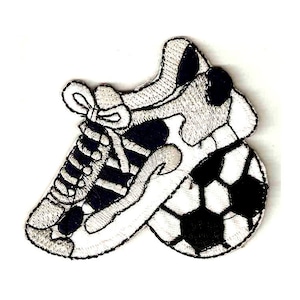 Könnte beinhalten: Schwarz-weiß gestickter Aufnäher eines Sneakers mit einem Fußball. Der Sneaker hat Schnürsenkel und eine weiße Sohle. Der Fußball ist schwarz-weiß.