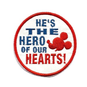 May include: A white, red and blue embroidered patch with a Mickey Mouse silhouette and the text "He's the hero of our hearts!"