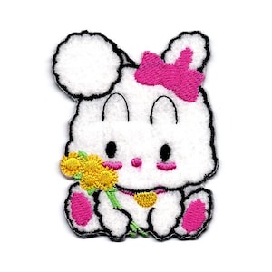 May include: White embroidered patch of a cartoon bunny holding a yellow flower. The bunny has a pink bow and pink feet.