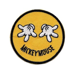 Può includere: Toppa ricamata gialla con un viso sorridente fatto dalle mani guantate bianche di Topolino e il testo "MICKEY MOUSE" in nero.