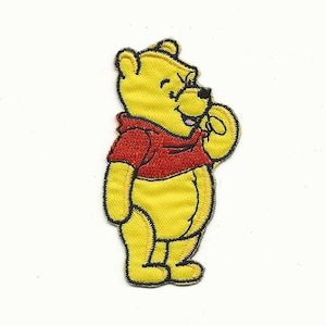 May include: An embroidered iron-on patch featuring Winnie the Pooh, a cartoon bear, in a red shirt. He is standing with his right paw raised to his mouth, looking to the right.