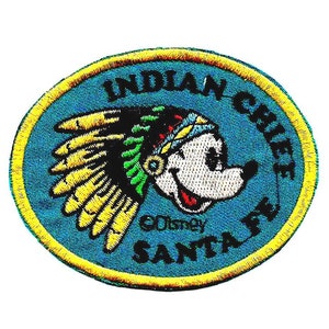 May include: Embroidered patch featuring Mickey Mouse in a Native American headdress. The patch is oval-shaped with a blue background and yellow border. Text includes "INDIAN CHIEF SANTA FE" and "©Disney".