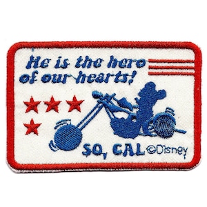 Puede incluir: Parche bordado con borde rojo y fondo blanco. El parche presenta una silueta azul de un personaje montando una motocicleta, con el texto "He is the hero of our hearts!" y "SO, CAL ©Disney". Hay tres estrellas rojas.