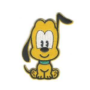 Op de afbeelding: Een geborduurde patch met een gele cartoon-hond met zwarte oren en een groene halsband. De hond heeft witte ogen en een zwarte neus.