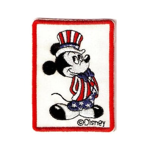 Puede incluir: Parche bordado con Mickey Mouse con atuendo patriótico. Mickey lleva un sombrero y un atuendo del Tío Sam rojo, blanco y azul. El parche tiene un borde rojo y el logotipo de Disney.