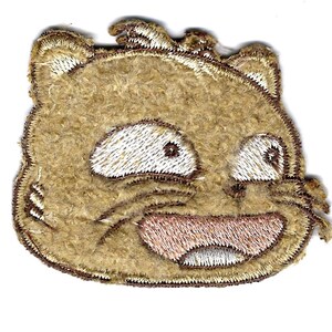 May include: A brown embroidered patch of a cartoon cat with a wide open mouth and big eyes. The cat is smiling with its tongue sticking out.