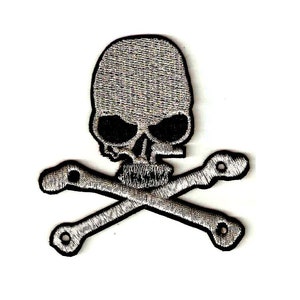 May include: A silver embroidered skull and crossbones patch. The skull is detailed with black eyes and a black mouth.