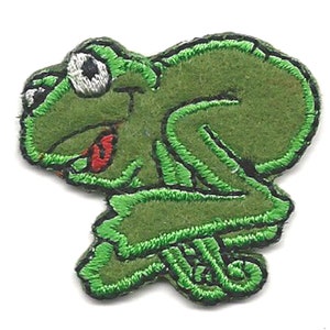 Może przedstawiać: Aplikacja żaby z zielonego filcu z haftowanymi detalami. Żaba ma duże, okrągłe oko i szeroko otwarte usta.