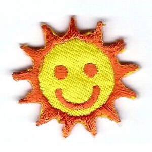 May include: A yellow smiling sun with an orange embroidered outline. The sun has a happy face with two eyes and a wide smile.