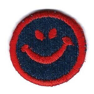 May include: A red embroidered smiley face patch on a blue denim background.
