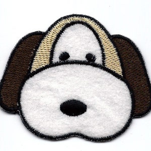 Könnte beinhalten: Ein weißer Filz-Aufnäher eines Hundes mit braunen Ohren und einem beigefarbenen Umriss. Der Hund hat schwarze Augen und eine schwarze Nase.