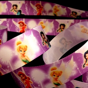 May include: Purple satin ribbon with a repeating pattern of Tinkerbell and other fairies. The fairies are surrounded by sparkling stars and glitter.