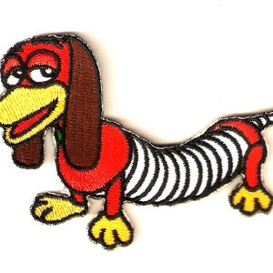 May include: A red and white striped dachshund dog with brown ears and yellow feet. The dog is smiling and has a green collar.