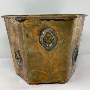 May include: Octagonal brass planter with an aged patina and intricate floral designs. The planter has decorative accents on each side.