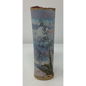 May include: A tall, cylindrical ceramic vase with a textured, rough rim. The vase features a painted landscape with a full moon, clouds, and a tree branch design. The color palette includes blues, purples, and earth tones.
