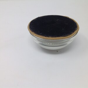 May include: A small, clear glass bowl with a black velvet lining and a gold trim around the top.