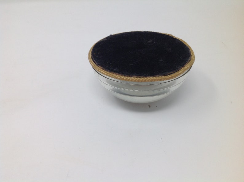 May include: A small, clear glass bowl with a black velvet lining and a gold trim around the top.