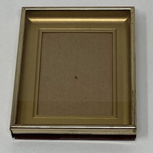 May include: A gold picture frame with a brown mat. The frame has a simple, classic design.