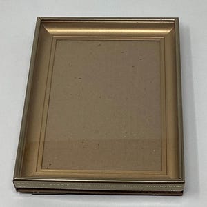 May include: A gold picture frame with a simple design. The frame has a beveled edge and a decorative border.