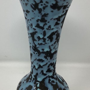 May include: A small, blue and black ceramic vase with a speckled glaze. The vase has a round base and a narrow neck.