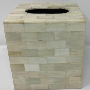 May include: A white tissue box cover made of bone inlay tiles. The tiles are arranged in a brick pattern. The box has a rectangular opening on the top for tissues.