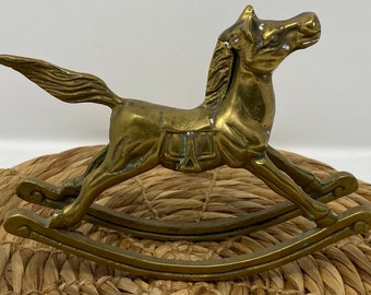 May include: A brass rocking horse figurine with a saddle and a detailed mane. The horse is on a rocking base and is a vintage style.