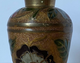 May include: A small brass vase with a gold, brown, green, white, and red floral design. The vase has a flared top and a round body.