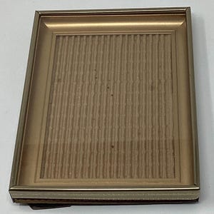 May include: A gold-colored picture frame with a textured cardboard backing. The frame has a simple, classic design.