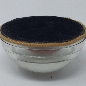 May include: A silver-coloured, round, metal container with a black velvet lining and a gold trim around the top.