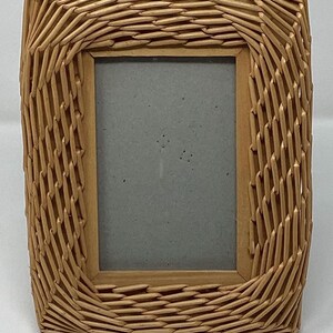 May include: A natural woven wicker picture frame with a light brown color. The frame has a rectangular shape with rounded corners.