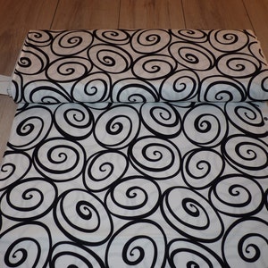 Può includere: Tessuto bianco con un motivo a spirale nero. Il tessuto è piegato a metà e il motivo è visibile su entrambi i lati.