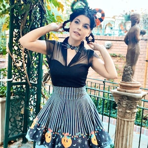 May include: A woman wearing a black and white striped skirt with a pumpkin and Christmas lights print. The skirt has a black bow and a black mesh top. She is wearing a wreath and a candy cane headband.