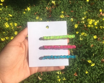 May include: Three beaded hair clips in green, pink, and blue. The clips are on a white card.