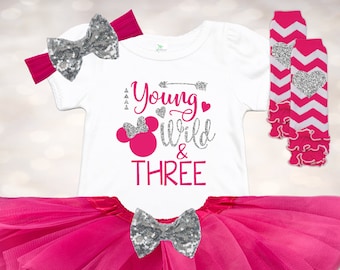 Può includere: Una gonna tutu in tulle rosa con un fiocco di paillettes argentate, una maglietta bianca con il testo "Young Wild & THREE" e una testa di Topolino in paillettes argentate, e un paio di scaldagambe a righe rosa e bianche con cuori argentati scintillanti.
