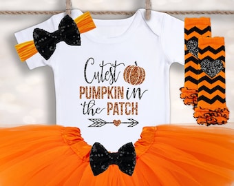 May include: Orange tulle tutu skirt with a black bow, a white bodysuit with the text "Cutest Pumpkin in the Patch" and a pumpkin graphic, and black and orange leg warmers with a heart design.