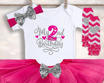 May include: A pink tutu, white bodysuit with silver glitter text that says "My 2nd Birthday", a silver glitter bow, and pink and white leg warmers with a silver heart.